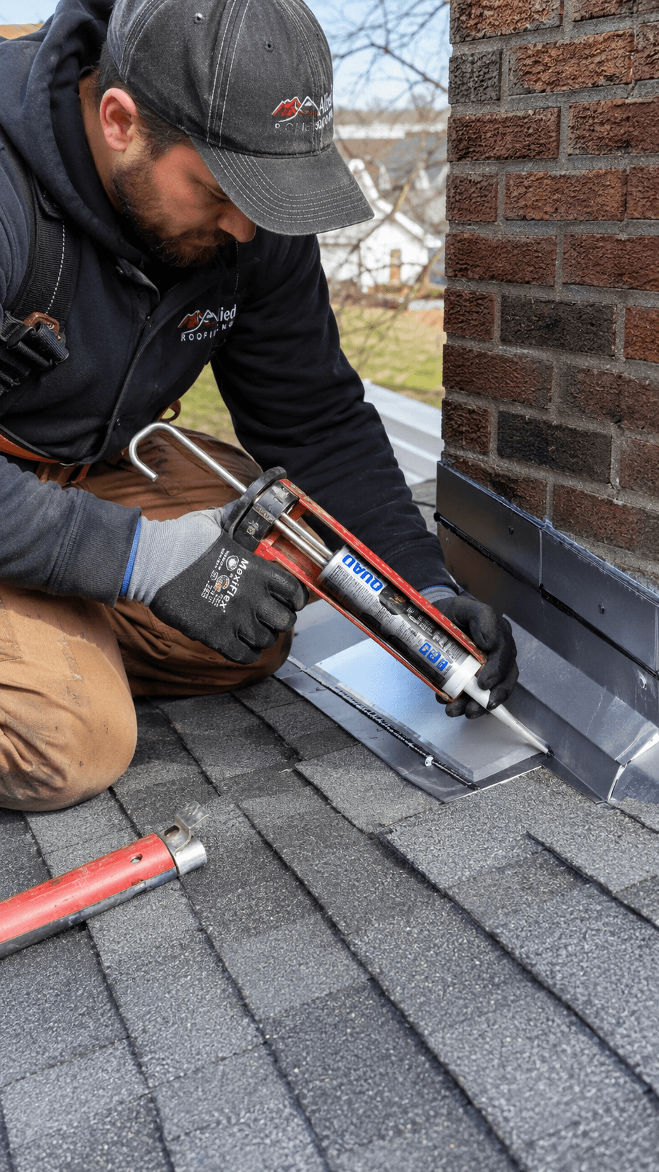 Roofer sealing metal flashing where the roof meets a brick chimney